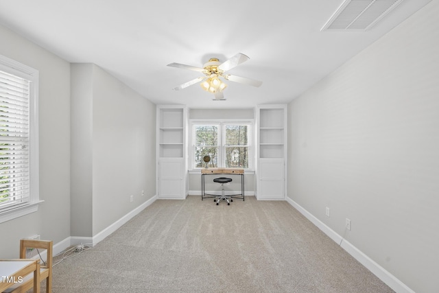 unfurnished office featuring built in shelves, light carpet, a ceiling fan, visible vents, and baseboards