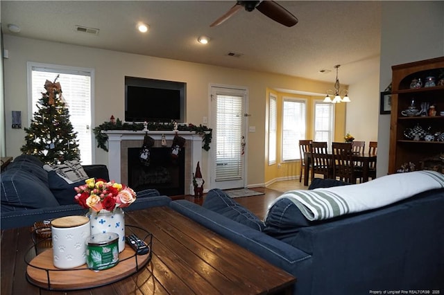 living room featuring hardwood / wood-style flooring, ceiling fan with notable chandelier, plenty of natural light, and a fireplace