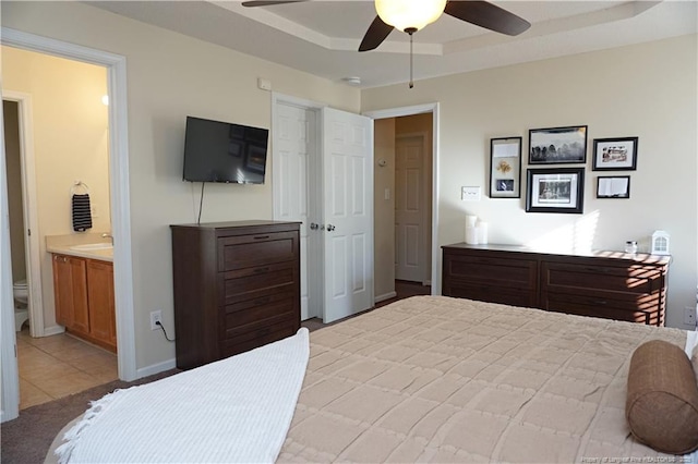 bedroom featuring ceiling fan, light tile patterned floors, connected bathroom, and a tray ceiling