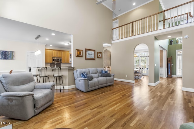 living room featuring ceiling fan, light hardwood / wood-style flooring, crown molding, and a towering ceiling