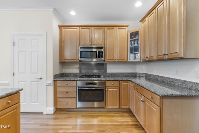 kitchen featuring appliances with stainless steel finishes, light hardwood / wood-style flooring, crown molding, and dark stone countertops