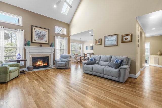 living room featuring a skylight, light wood-type flooring, a towering ceiling, and ceiling fan