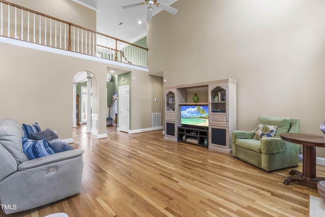 living room featuring a towering ceiling, ceiling fan, ornate columns, and wood-type flooring