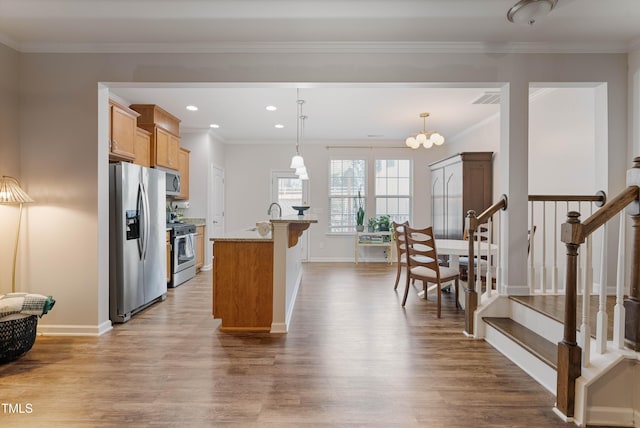 kitchen with decorative light fixtures, a center island with sink, crown molding, stainless steel appliances, and light stone counters