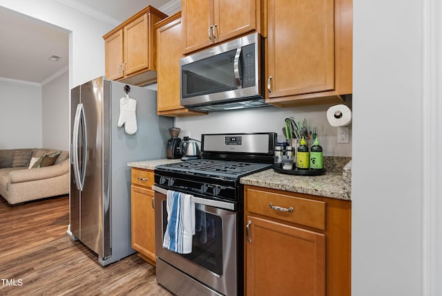 kitchen featuring light stone counters, crown molding, stainless steel appliances, and light wood-type flooring