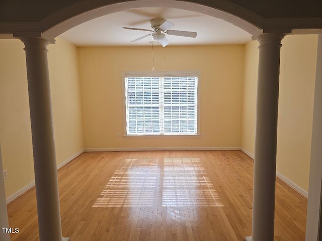 empty room featuring light wood-type flooring, ceiling fan, and ornate columns