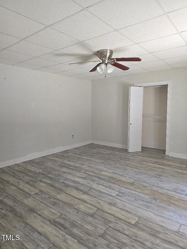 unfurnished bedroom featuring ceiling fan, a paneled ceiling, a closet, and wood-type flooring