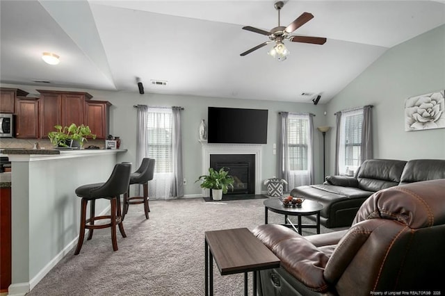 living room with visible vents, light colored carpet, lofted ceiling, a fireplace with flush hearth, and ceiling fan