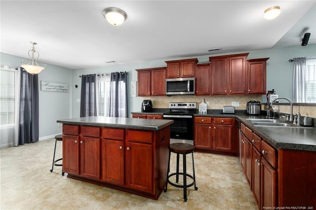 kitchen with a breakfast bar, a sink, appliances with stainless steel finishes, tasteful backsplash, and dark countertops