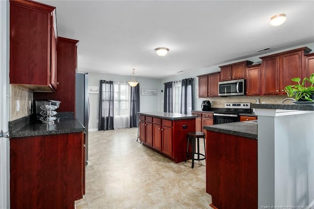 kitchen with reddish brown cabinets, dark countertops, a center island, stainless steel appliances, and backsplash