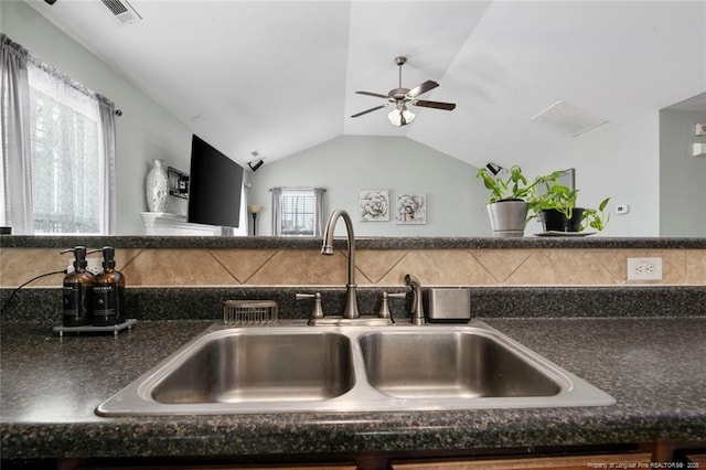 kitchen featuring visible vents, dark countertops, ceiling fan, vaulted ceiling, and a sink