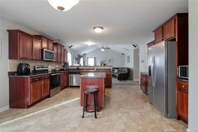 kitchen with a breakfast bar area, stainless steel appliances, a peninsula, vaulted ceiling, and dark countertops