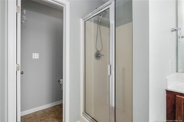 bathroom featuring tile patterned flooring, baseboards, a shower stall, and vanity