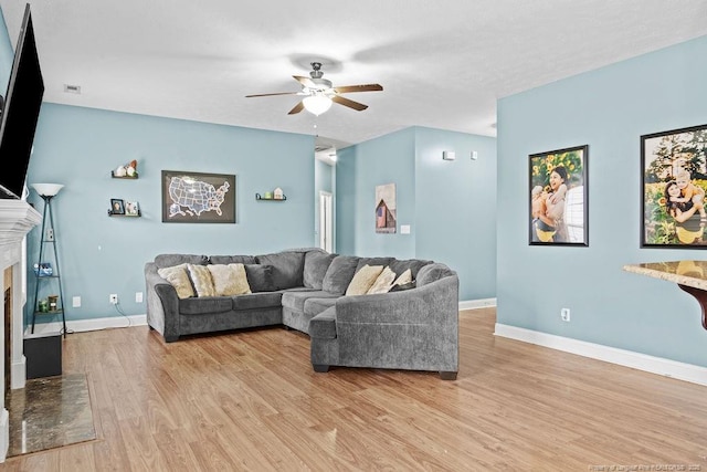 living room with a high end fireplace, light hardwood / wood-style floors, and ceiling fan