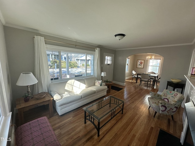 living room with wood finished floors, arched walkways, crown molding, baseboards, and a chandelier