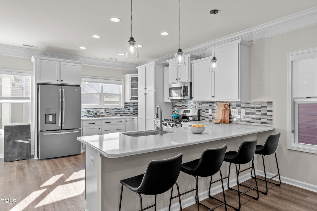 kitchen with kitchen peninsula, appliances with stainless steel finishes, sink, pendant lighting, and white cabinets