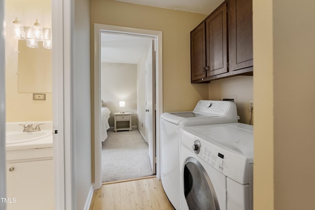 laundry area with washing machine and dryer, sink, light hardwood / wood-style floors, and cabinets