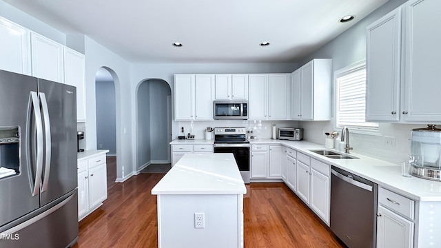 kitchen with white cabinets, appliances with stainless steel finishes, a kitchen island, tasteful backsplash, and sink