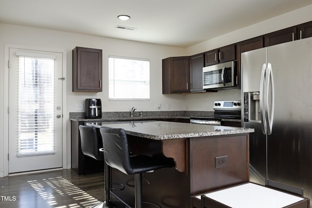 kitchen featuring a healthy amount of sunlight, appliances with stainless steel finishes, a center island, and dark brown cabinetry