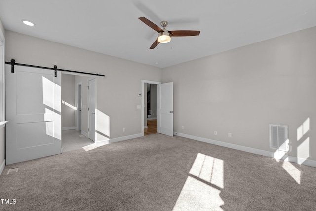 unfurnished bedroom with ceiling fan, light carpet, and a barn door