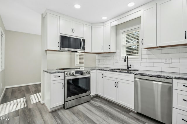 kitchen featuring sink, light hardwood / wood-style flooring, appliances with stainless steel finishes, white cabinets, and dark stone counters