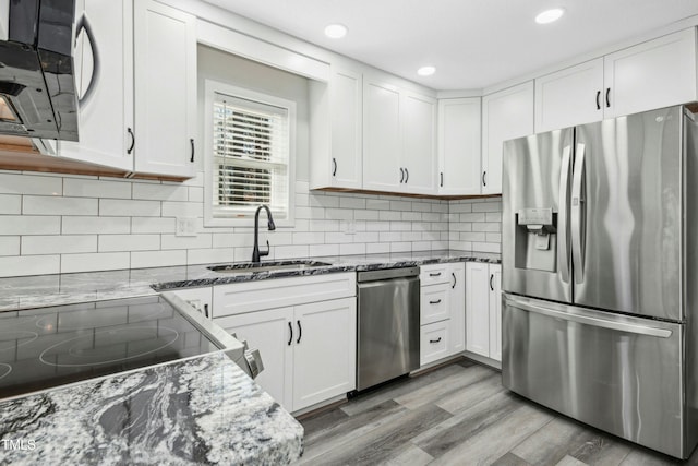 kitchen with dark stone countertops, wood-type flooring, sink, white cabinetry, and appliances with stainless steel finishes