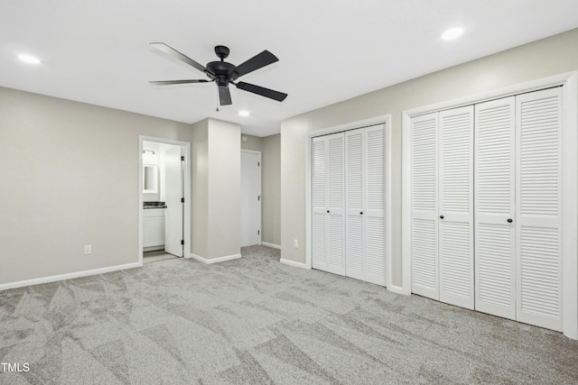 unfurnished bedroom featuring ceiling fan, light colored carpet, ensuite bathroom, and multiple closets