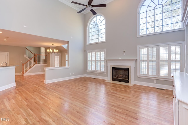 unfurnished living room with a high ceiling, ornamental molding, ceiling fan with notable chandelier, and light hardwood / wood-style flooring