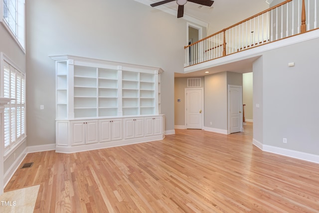 unfurnished living room with light hardwood / wood-style floors, ceiling fan, and a high ceiling