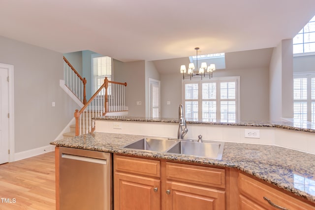 kitchen featuring sink, light hardwood / wood-style flooring, hanging light fixtures, light stone countertops, and stainless steel dishwasher