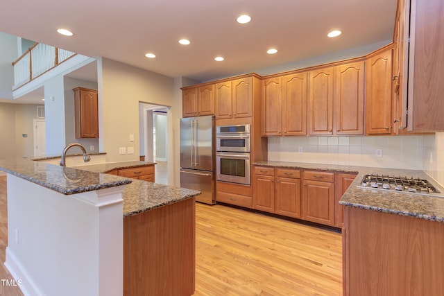 kitchen with appliances with stainless steel finishes, dark stone countertops, backsplash, kitchen peninsula, and light wood-type flooring