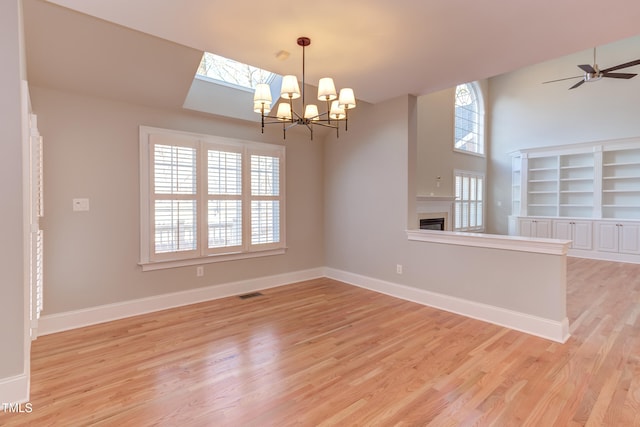 unfurnished room featuring light hardwood / wood-style flooring, built in shelves, plenty of natural light, and ceiling fan with notable chandelier