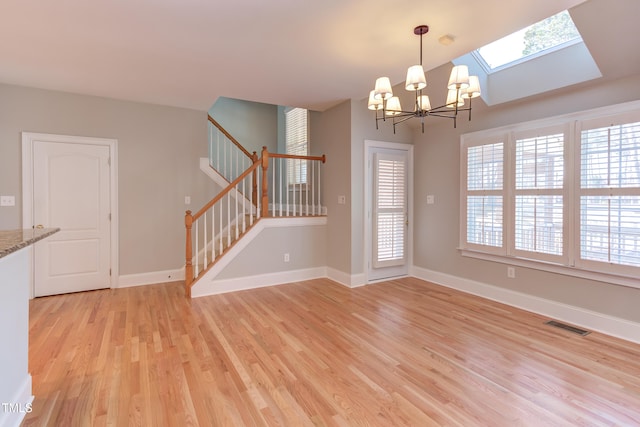 unfurnished dining area with a notable chandelier, light wood-type flooring, and a skylight