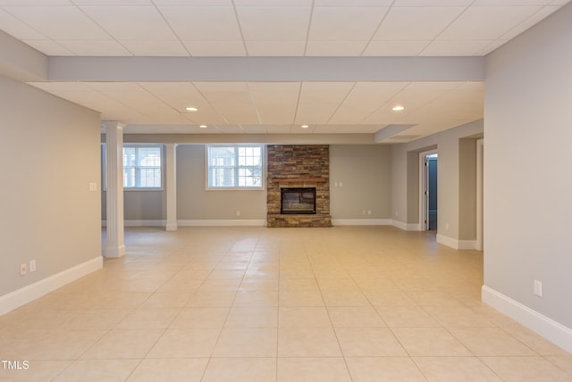 unfurnished living room featuring a stone fireplace, light tile patterned floors, and a drop ceiling