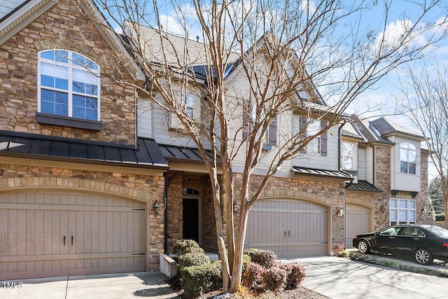 view of property featuring a standing seam roof, metal roof, a garage, stone siding, and driveway