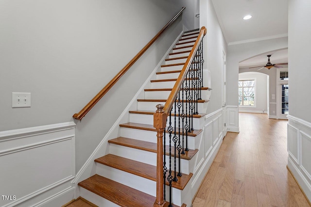 stairs with arched walkways, wainscoting, ornamental molding, wood finished floors, and a decorative wall