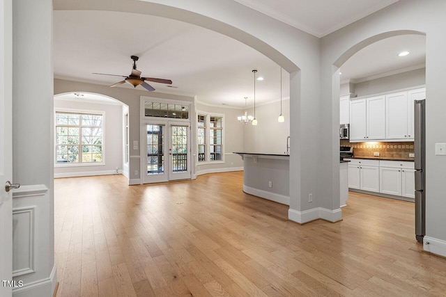 unfurnished living room featuring ceiling fan with notable chandelier, light hardwood / wood-style floors, crown molding, and french doors