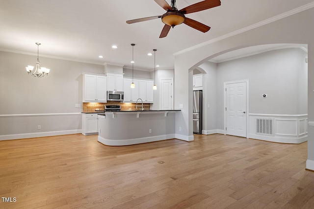 kitchen with appliances with stainless steel finishes, pendant lighting, white cabinets, ceiling fan with notable chandelier, and ornamental molding