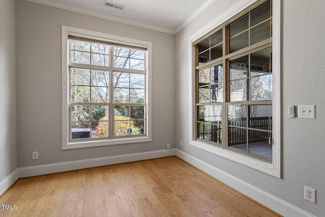 empty room with light wood-type flooring, visible vents, crown molding, and baseboards