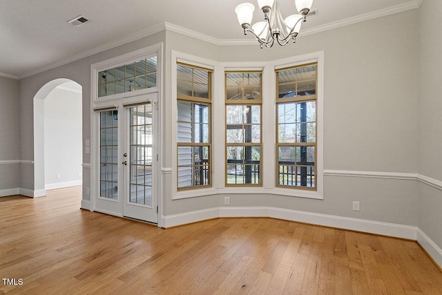 unfurnished dining area with arched walkways, wood finished floors, visible vents, baseboards, and crown molding