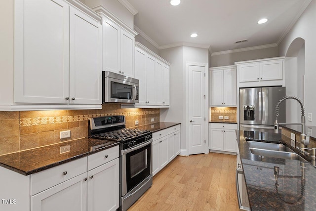 kitchen featuring white cabinets, appliances with stainless steel finishes, crown molding, light wood-type flooring, and a sink