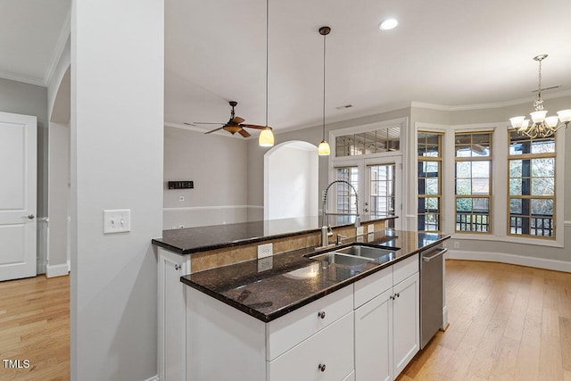 kitchen with stainless steel dishwasher, ornamental molding, a sink, dark stone countertops, and light wood-type flooring