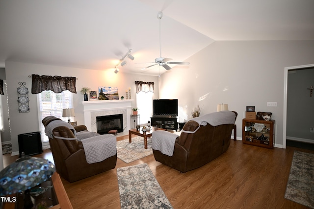 living room featuring dark hardwood / wood-style floors, a premium fireplace, lofted ceiling, rail lighting, and ceiling fan