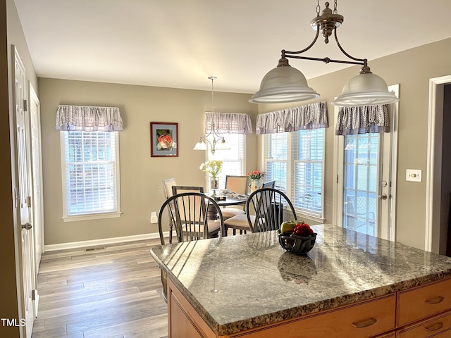 kitchen featuring baseboards, light wood-style floors, brown cabinets, a center island, and dark stone countertops