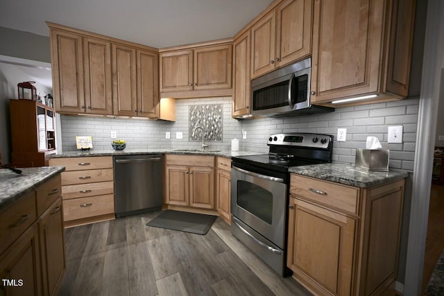 kitchen featuring stainless steel appliances, dark wood finished floors, stone counters, and a sink