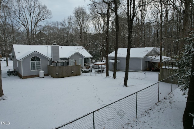 snow covered back of property with a chimney and fence