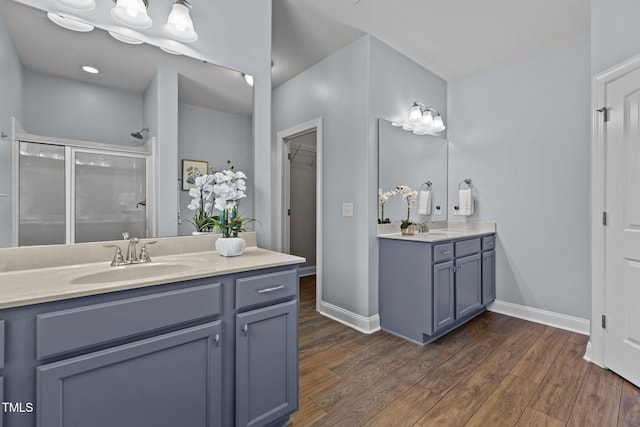 bathroom with a stall shower, two vanities, a sink, and wood finished floors