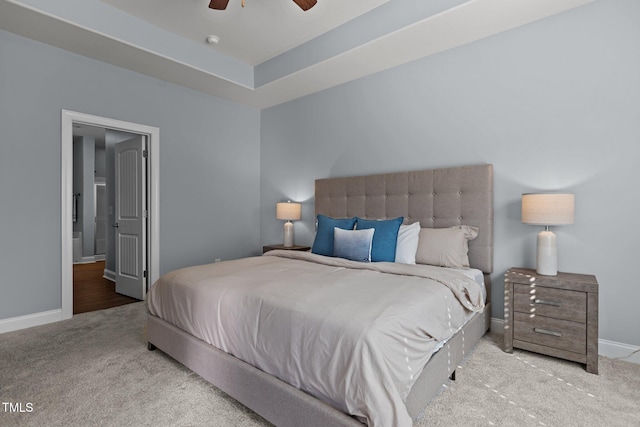 carpeted bedroom featuring ceiling fan, a raised ceiling, and baseboards