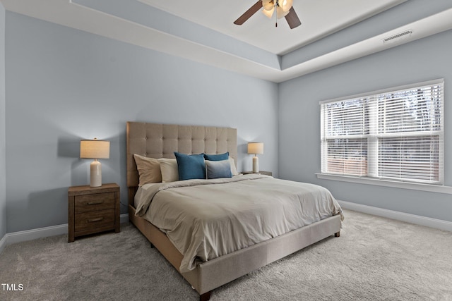 carpeted bedroom featuring a ceiling fan, a raised ceiling, visible vents, and baseboards