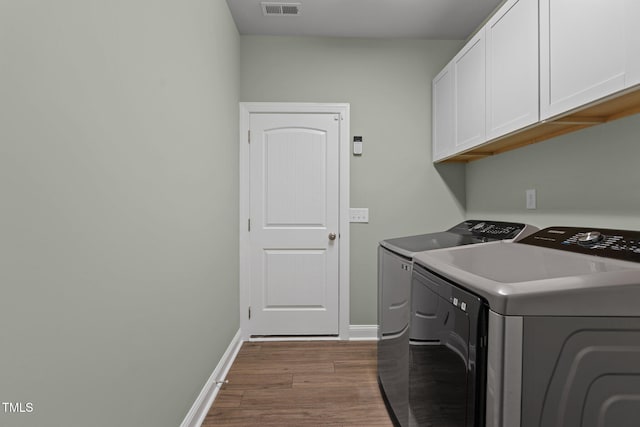 washroom featuring washing machine and clothes dryer, visible vents, baseboards, cabinet space, and dark wood finished floors